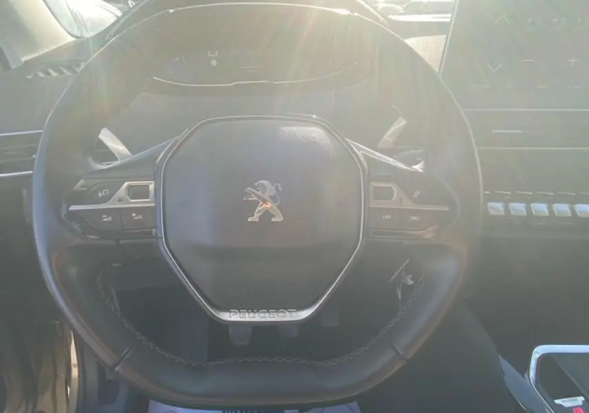 Vue rapprochée du volant compact noir de la Peugeot 3008 beige clair, avec commandes multifonctions visibles.
