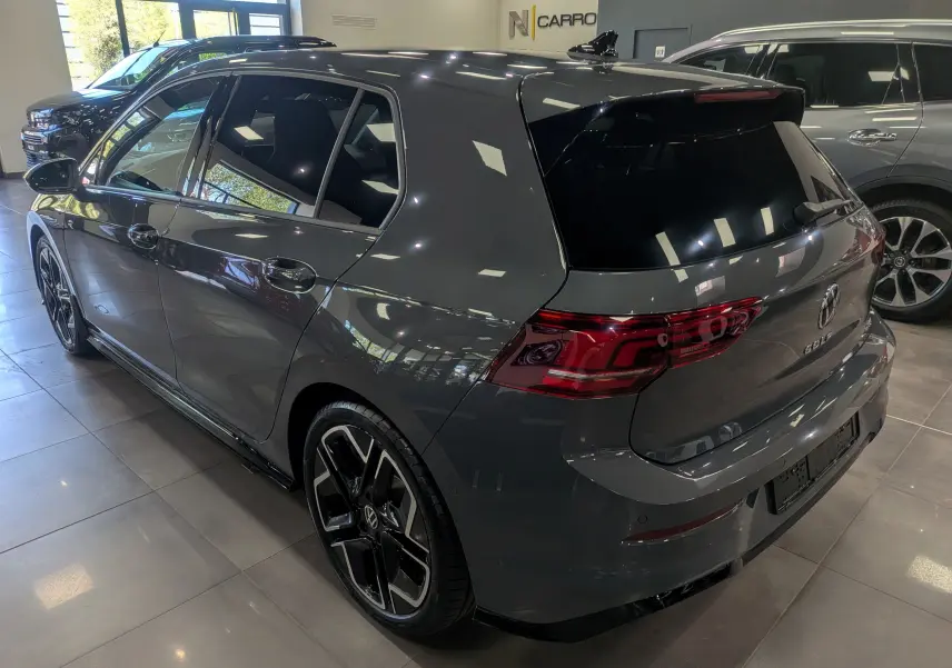 Volkswagen Golf VIII gris Urano vue 3/4 arrière droit en intérieur, avec jantes noires bi-ton et vitres teintées.