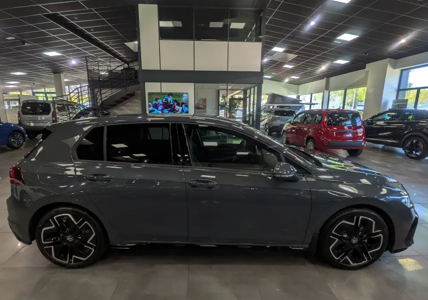 Volkswagen Golf VIII 1.5 eTSI R-Line gris Urano vue de profil côté gauche en intérieur showroom.