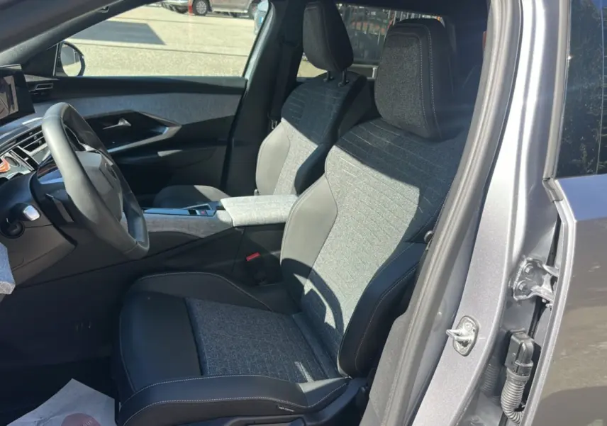 Vue intérieure côté conducteur du Peugeot 5008 Hybrid gris artense, sièges cuir tissu et accoudoir central visible.