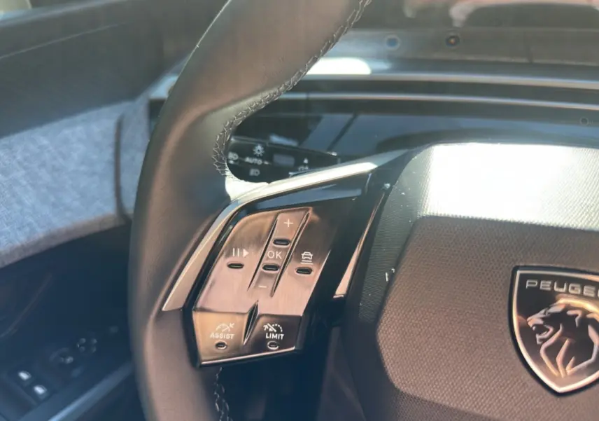 Gros plan sur le volant cuir noir du Peugeot 5008 Hybrid 145, avec commandes multifonctions et logo lion central.