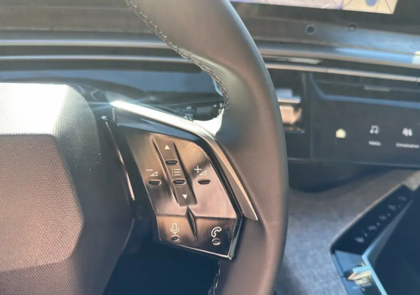 Gros plan sur le volant cuir multifonctions de la Peugeot 5008 gris artense, avec commandes vocales et audio visibles.