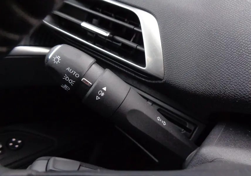 Gros plan sur la commande des feux et clignotants à gauche du tableau de bord noir du Peugeot 3008 gris Artense 2023.