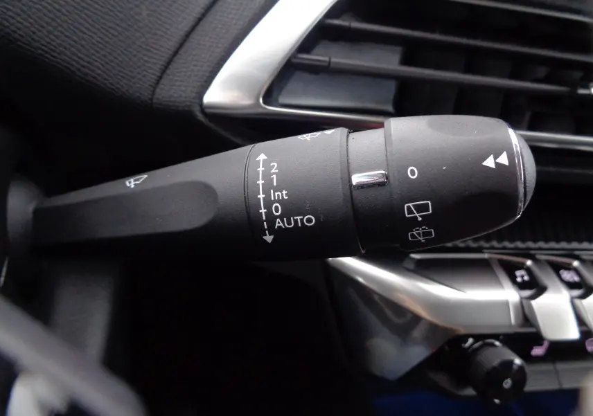 Gros plan sur la manette d'essuie-glace du Peugeot 3008 2023, avec commandes blanches sur fond noir et tableau de bord gris.
