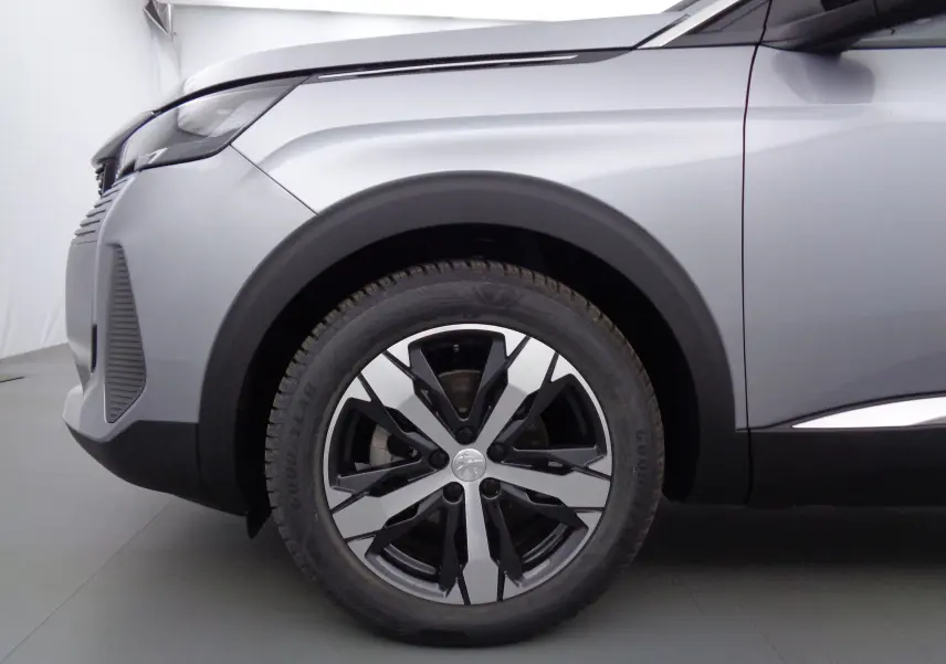 Gros plan sur la roue avant gauche d'un Peugeot 3008 gris Artense métal 2023 avec jante alliage bicolore.
