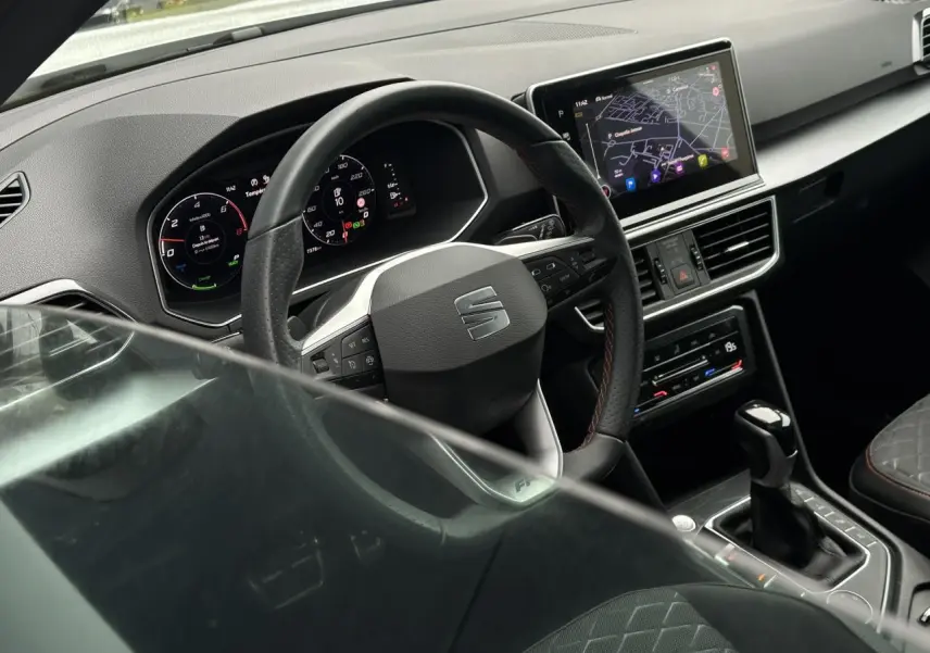 Vue intérieure du poste de conduite du SEAT Tarraco blanc, volant cuir multifonction et écran tactile de navigation visible.