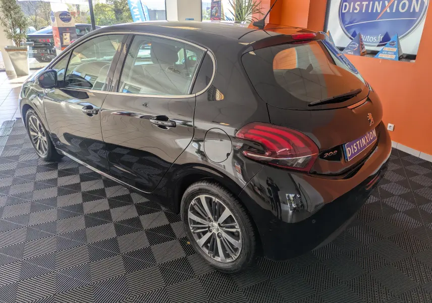 Peugeot 208 Allure noire vue 3/4 arrière droit en intérieur, avec jantes alliage et feux arrière distinctifs.