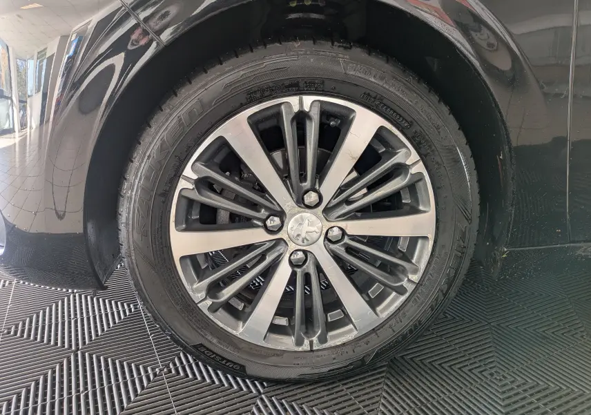 Gros plan sur la roue avant gauche noire d’une Peugeot 208 Allure 2019 avec jante alliage multibranches.