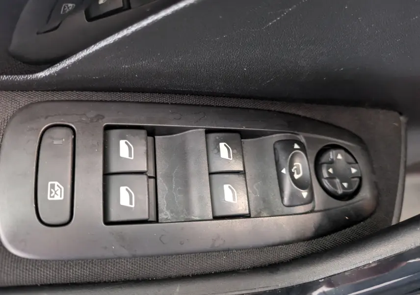Gros plan sur les commandes de lève-vitres et rétroviseurs côté conducteur d’une Peugeot 208 noire Allure 2019.