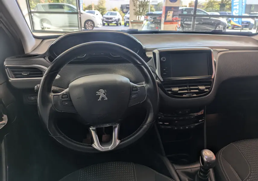 Intérieur de la Peugeot 208 Allure 2019, vue centrée sur le volant cuir noir et la console avec écran tactile.