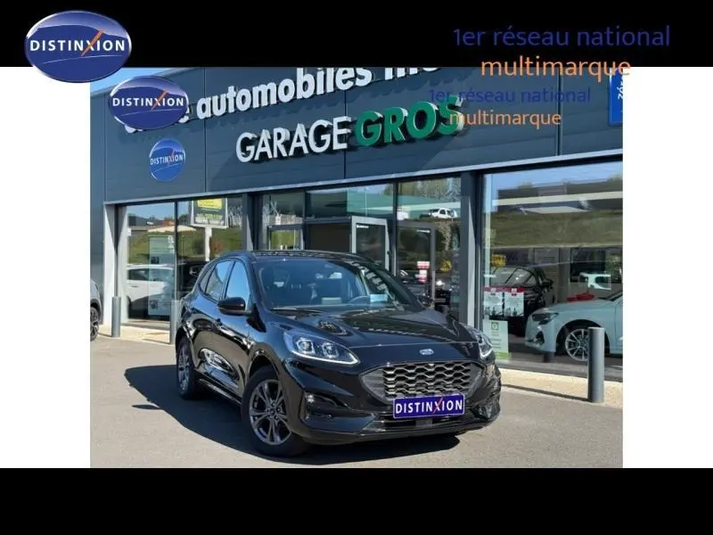 Ford Kuga 2024 noir Agate métallisé en 3/4 avant, avec calandre distinctive et jantes alu foncées, devant un garage multimarque.