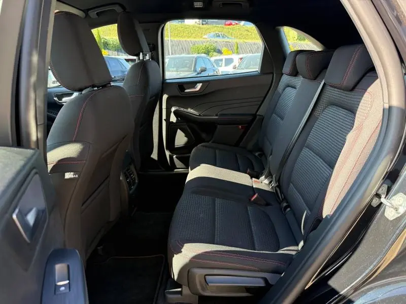 Vue latérale droite de l'habitacle arrière du Ford Kuga 2024 noir, sièges tissu noir avec surpiqûres rouges.