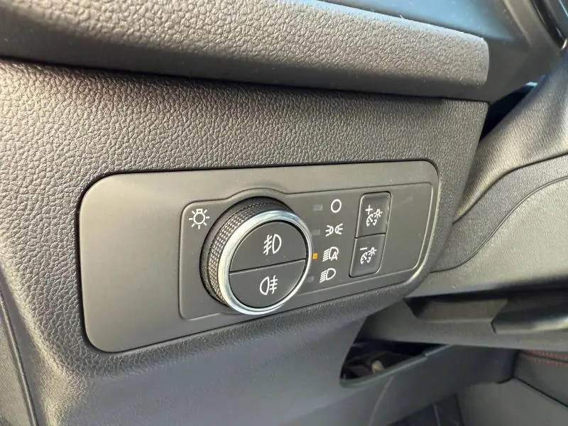 Gros plan sur le bouton de commande des phares et feux antibrouillard dans l'habitacle noir du Ford Kuga 2024.