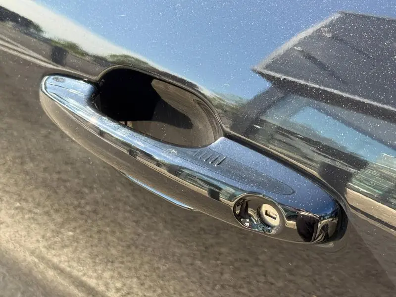 Gros plan sur la poignée de porte chromée du Ford Kuga noir Agate Métallisée, reflet de l'environnement visible.