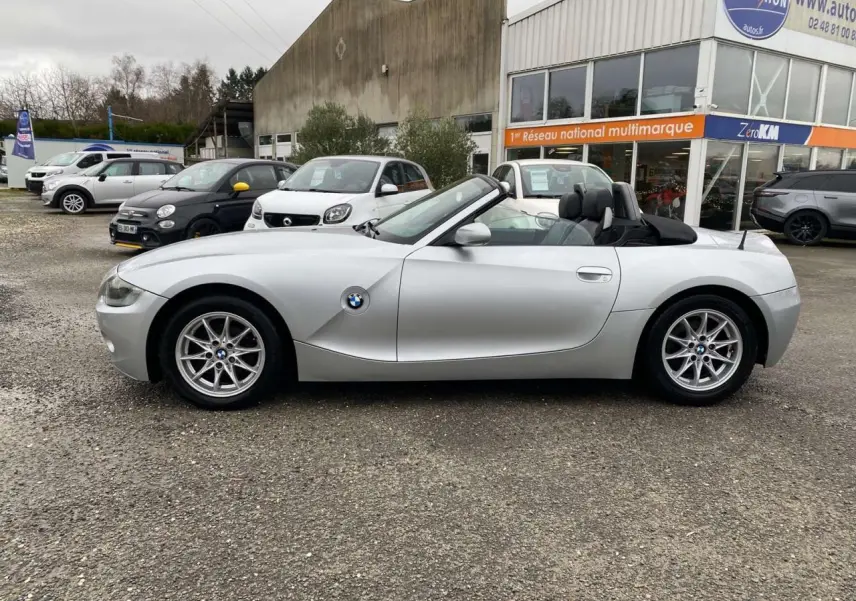 BMW Z4 Roadster gris clair vue de profil côté gauche, capote noire ouverte et jantes alliage 16 pouces visibles.