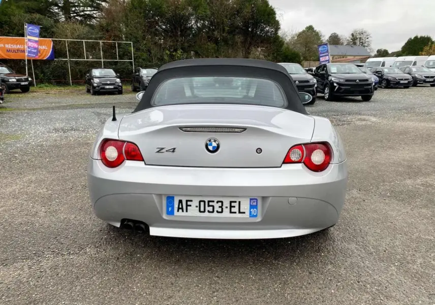 Vue arrière d'une BMW Z4 gris clair avec capote noire relevée et double sortie d'échappement visible.