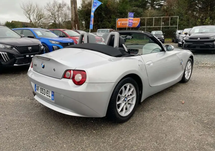BMW Z4 Roadster gris clair vue 3/4 arrière droit, capote noire fermée et jantes alliage 16 pouces visibles.