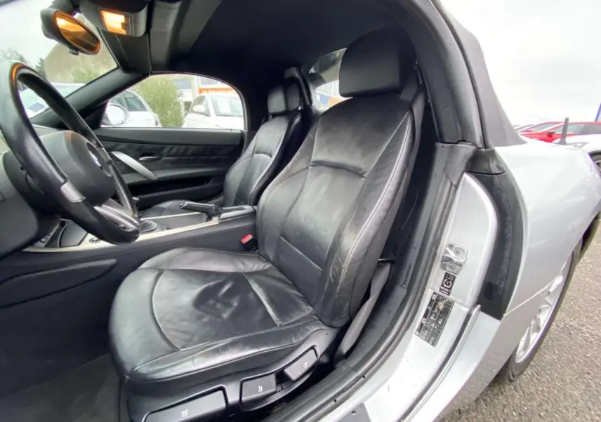 Vue intérieure côté conducteur d'une BMW Z4 Roadster gris clair de 2005 avec sièges cuir noirs et volant sport.