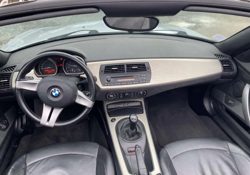 Vue intérieure avant de la BMW Z4 Roadster 2005, volant sport cuir, tableau de bord clair et levier de vitesse manuel.