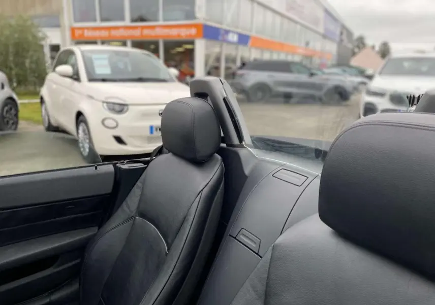 Vue intérieure rapprochée des sièges avant en cuir noir d’un BMW Z4 Roadster gris clair avec coupe-vent transparent.