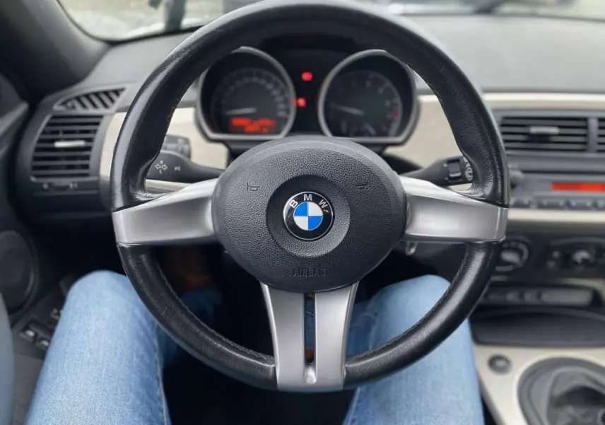 Vue intérieure centrée sur le volant sport cuir 3 branches de la BMW Z4 Roadster 2005, tableau de bord en arrière-plan.