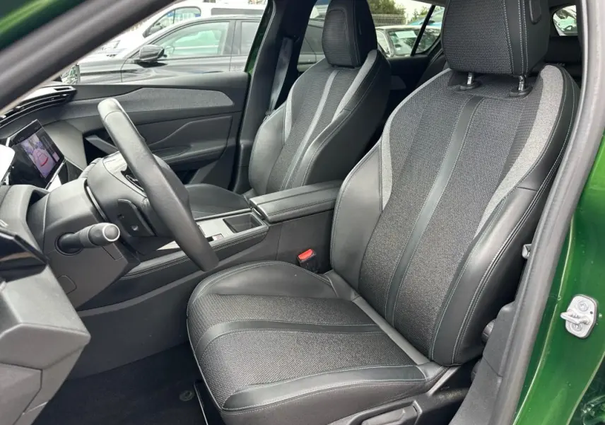 Vue intérieure côté conducteur de la Peugeot 308 2023 vert foncé, sièges tissu et cuir avec accoudoir central.