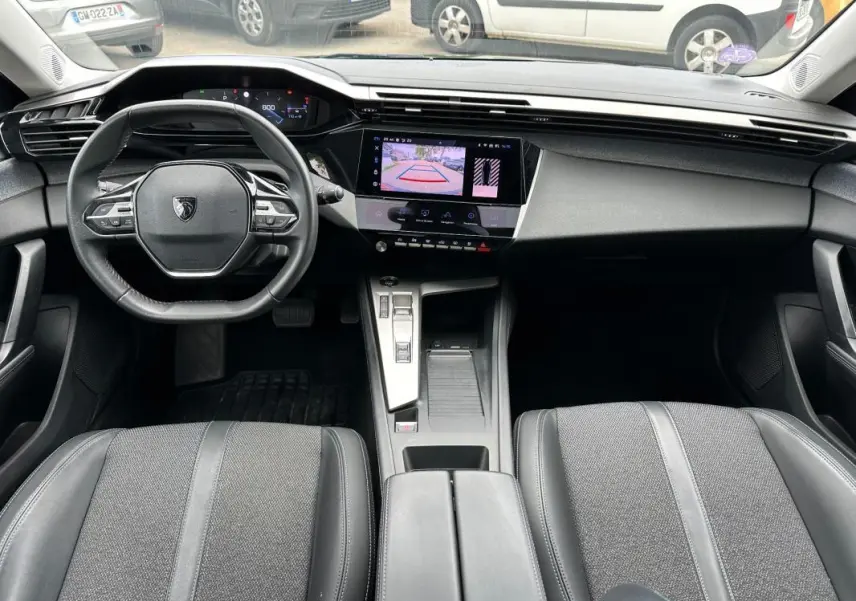 Vue intérieure avant de la Peugeot 308 2023, tableau de bord moderne avec écran tactile et volant compact noir.