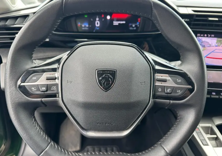 Vue rapprochée du volant noir de la Peugeot 308 2023 avec cockpit numérique et caméra de recul affichée.
