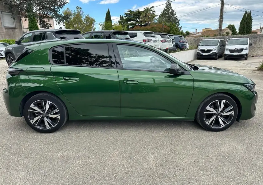Vue de profil côté gauche d'une Peugeot 308 2023 vert foncé avec jantes alliage 17 pouces sur parking.