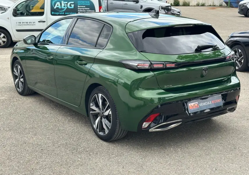 Vue 3/4 arrière droite d'une Peugeot 308 2023 vert foncé avec jantes alliage 17 pouces et feux arrière LED distinctifs.