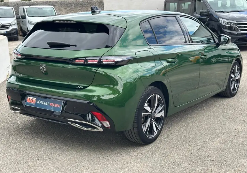 Vue 3/4 arrière droite d'une Peugeot 308 2023 vert foncé avec jantes alliage 17 pouces et vitres teintées.