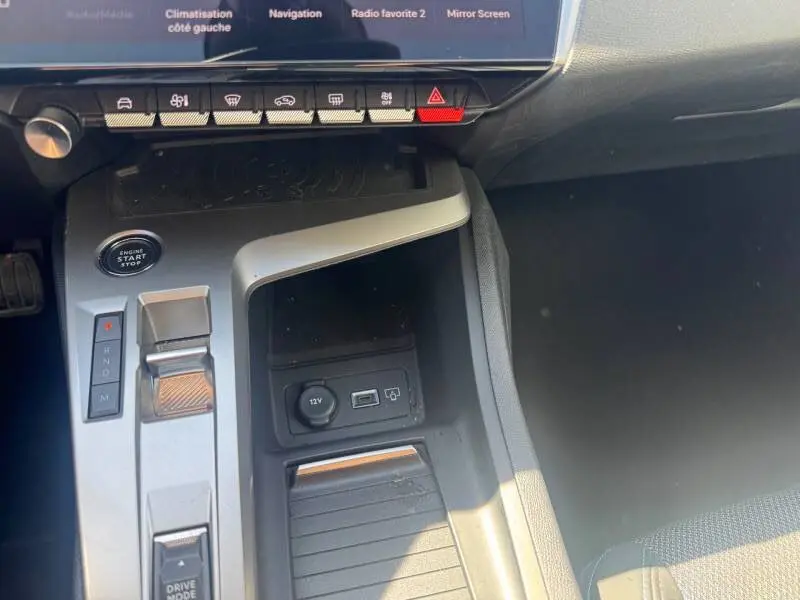 Vue rapprochée de la console centrale grise de la Peugeot 308 Hybrid 145 e-DCS6 Allure avec boutons de commande et prise USB visible.