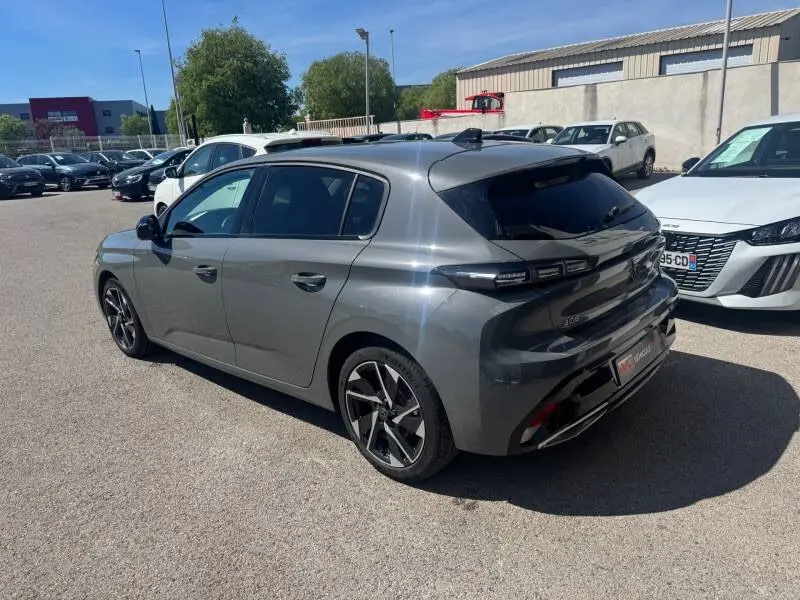 Peugeot 308 Hybrid gris vue 3/4 arrière droit, jantes alliage 17 pouces et vitres teintées visibles.