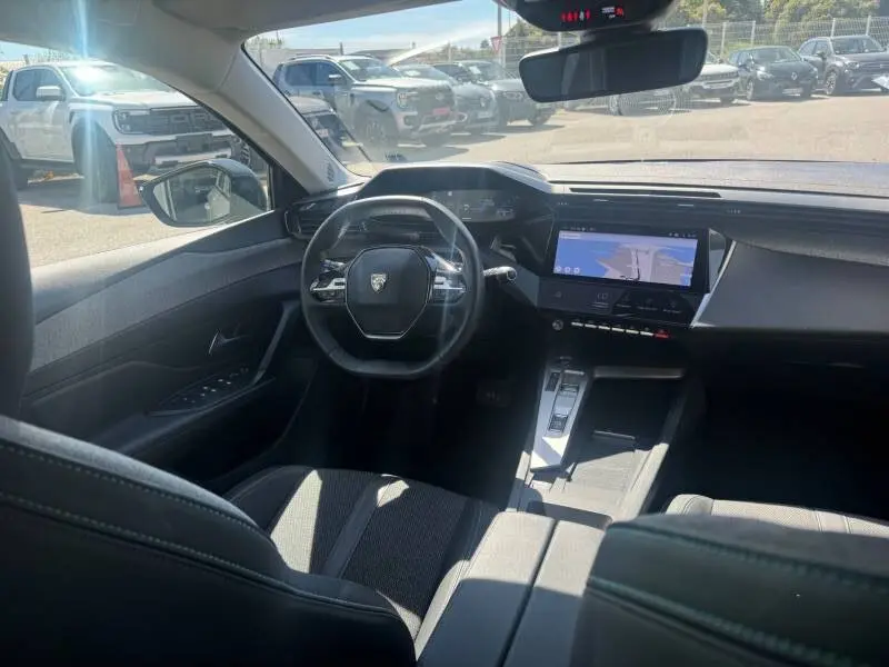 Vue intérieure avant droite du Peugeot 308 Hybrid 145 gris, avec cockpit numérique et écran tactile central allumé.