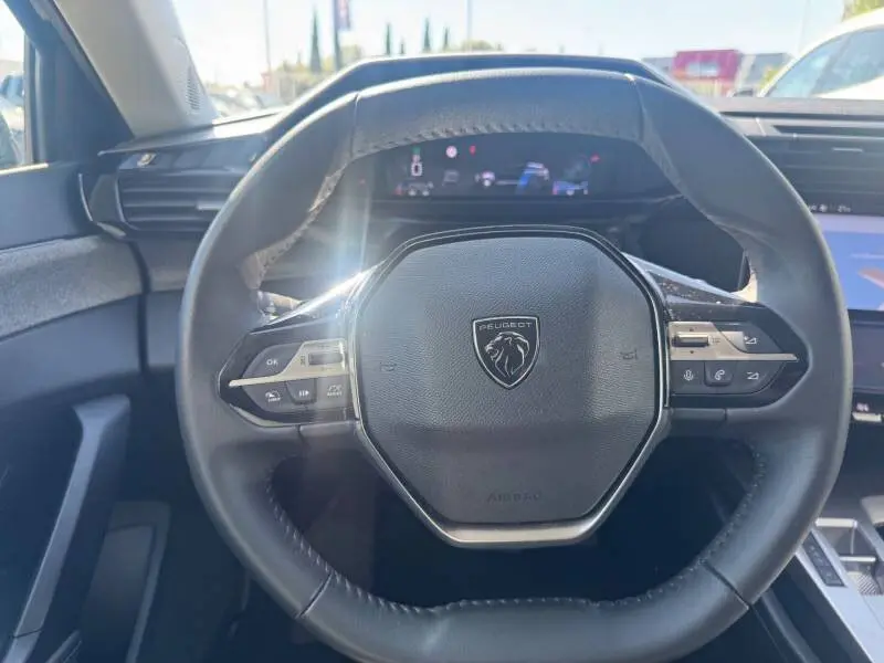 Vue rapprochée du volant cuir noir de la Peugeot 308 Hybrid 2025 avec commandes intégrées et tableau de bord numérique.