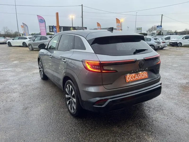 Vue 3/4 arrière droite d'un Renault Austral gris avec feux arrière LED allumés sur parking humide.