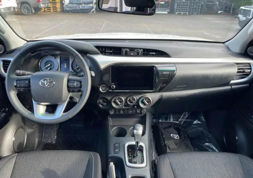 Intérieur du Toyota Hilux 2025 blanc, vue frontale sur le tableau de bord avec volant multifonction et console centrale.