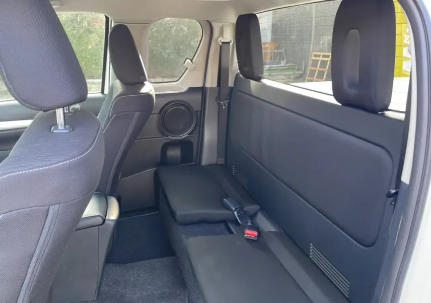 Intérieur arrière du Toyota Hilux 4x4 blanc pur 2025, vue côté droit sur les sièges noirs et la porte arrière ouverte.