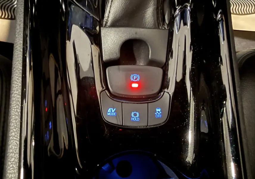 Gros plan sur la console centrale noire brillante du Toyota C-HR Hybride 2018, avec boutons EV Mode, Hold et frein à main électronique.