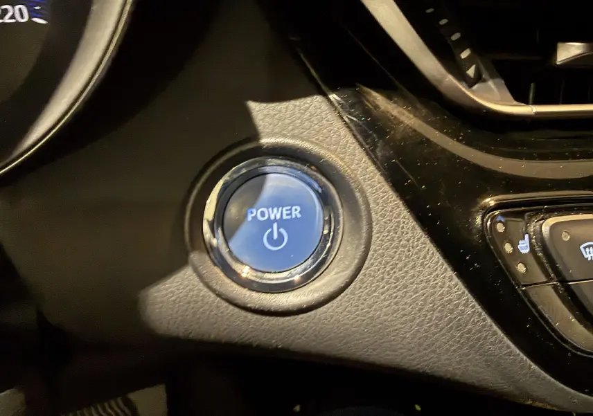 Bouton bleu Power en gros plan sur le tableau de bord noir du Toyota C-HR Hybride rouge, version 2018.