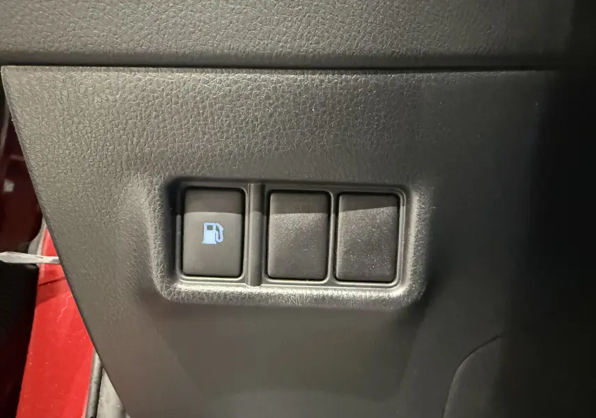 Gros plan sur le bouton d'ouverture du bouchon de carburant dans l'habitacle noir du Toyota C-HR Hybride rouge.