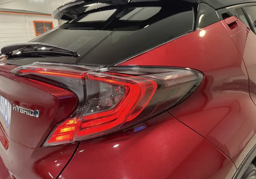 Vue arrière 3/4 droit du Toyota C-HR Hybride rouge, mettant en valeur le feu arrière et le badge Hybrid.