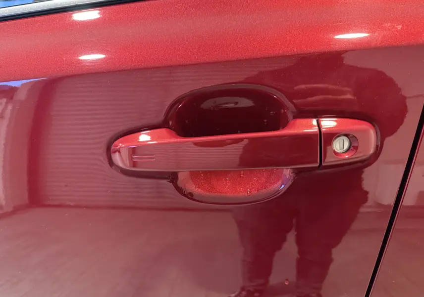 Poignée de porte rouge métallisée côté gauche d’un Toyota C-HR Hybride 2018, avec serrure intégrée visible.