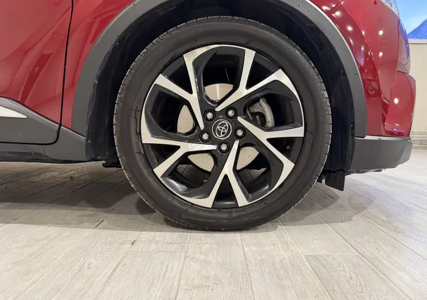 Gros plan sur la roue avant droite du Toyota C-HR hybride rouge, mettant en valeur la jante alliage bicolore au design dynamique.