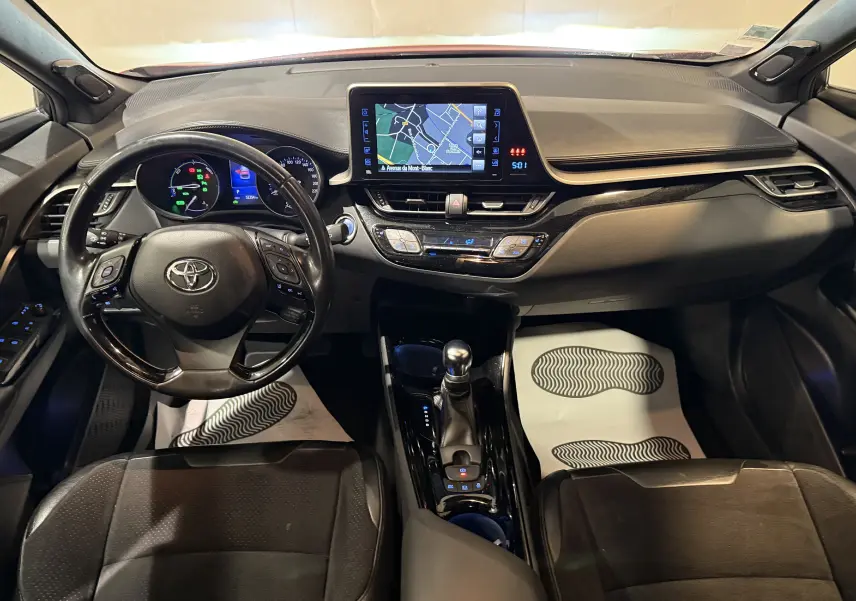 Vue intérieure avant du Toyota C-HR Hybride 2018, tableau de bord noir avec écran tactile et volant multifonction.