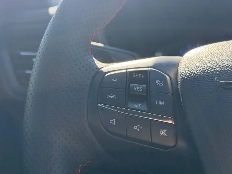 Gros plan sur le volant cuir perforé avec commandes multifonctions du Ford Kuga bleu 2024, version ST-Line.