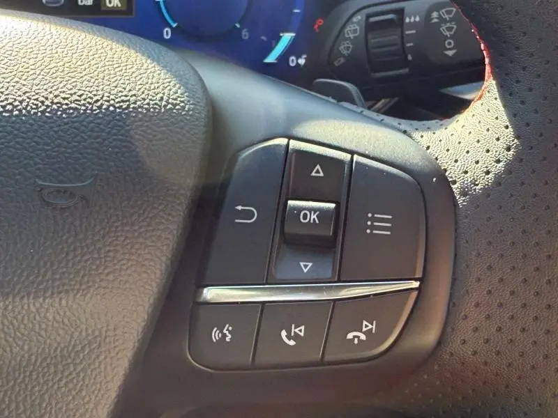 Gros plan sur les commandes multifonctions du volant cuir perforé côté gauche du Ford Kuga bleu 2024.