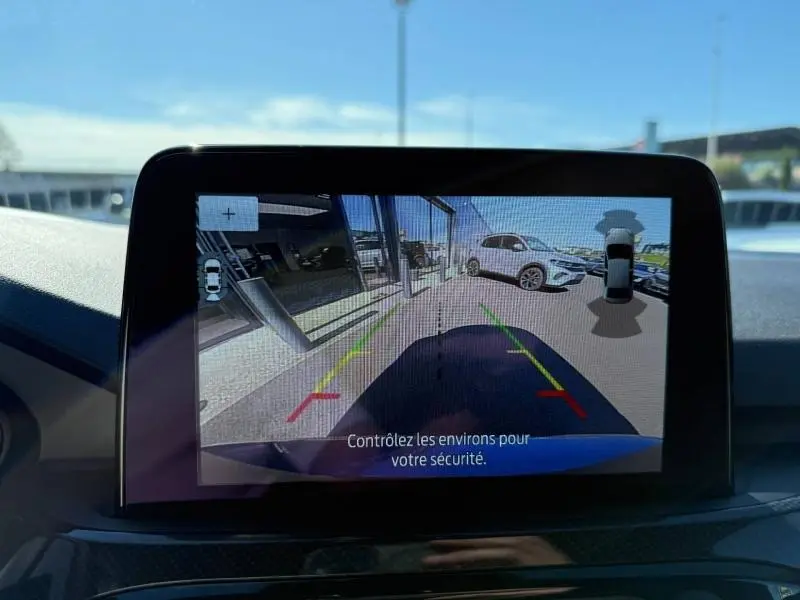 Écran de caméra de recul montrant l’arrière bleu du Ford Kuga 2024 avec repères de stationnement colorés.