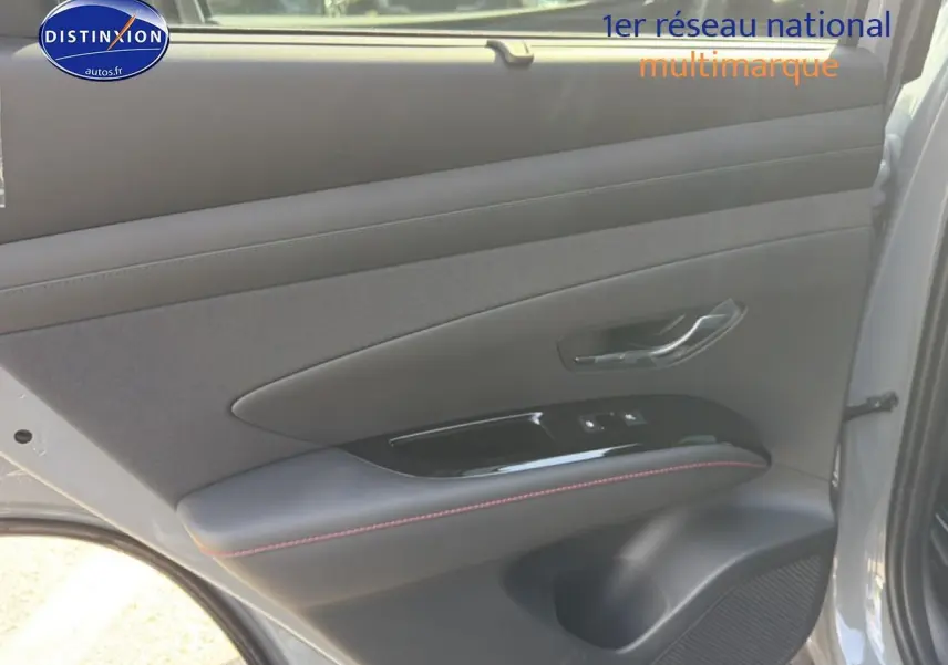 Vue intérieure côté gauche de la porte arrière gris shadow du Hyundai Tucson 2026 avec surpiqûres rouges et commandes vitres.