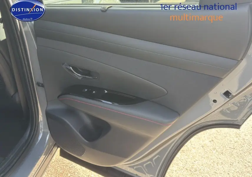 Vue intérieure du panneau de porte arrière droite gris shadow du Hyundai Tucson 2026 avec surpiqûres rouges et commande de vitres.